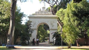 people on bycicles by an arch in Villa Borghese Rome